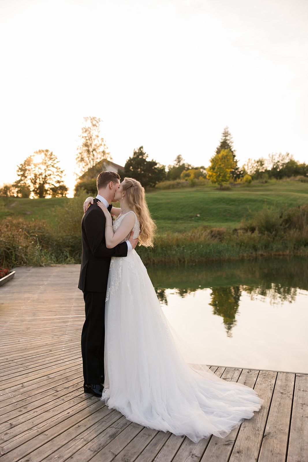 A couple shares a romantic moment on a wooden dock by a serene lake during golden hour sunset.