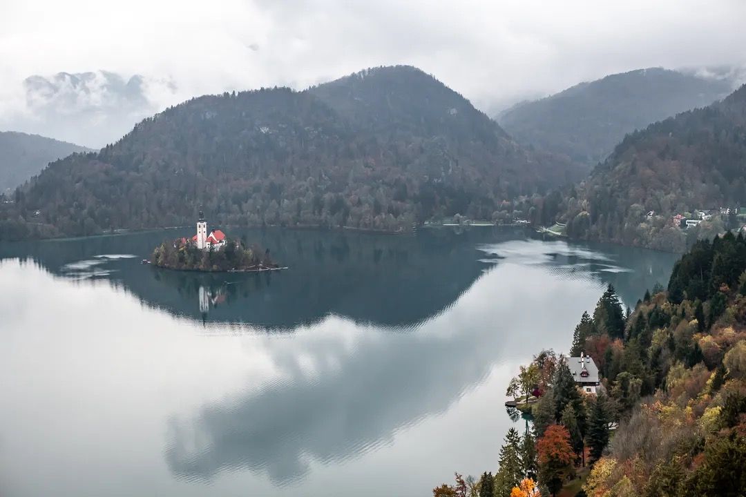 Lake Bled island and church reflected in still water with mountains behind.