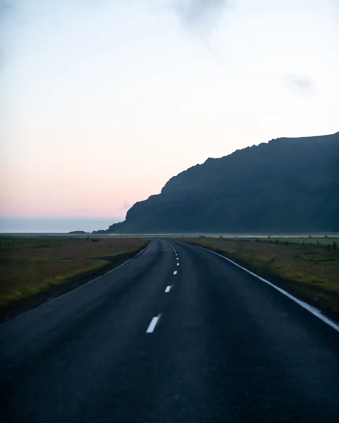 Quiet coastal road at sunset leading towards cliffs and the sea.