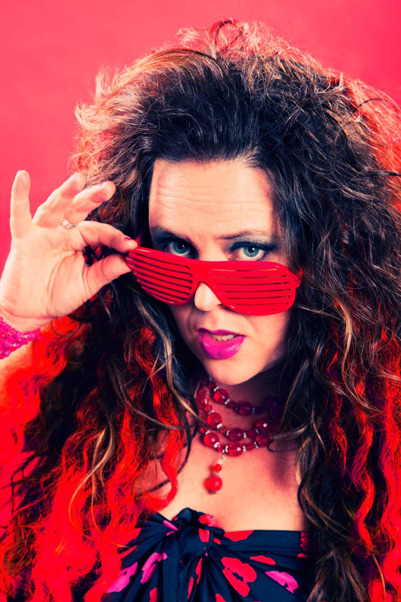 Artistic portrait with curly hair and red accessories against a bright pink backdrop.