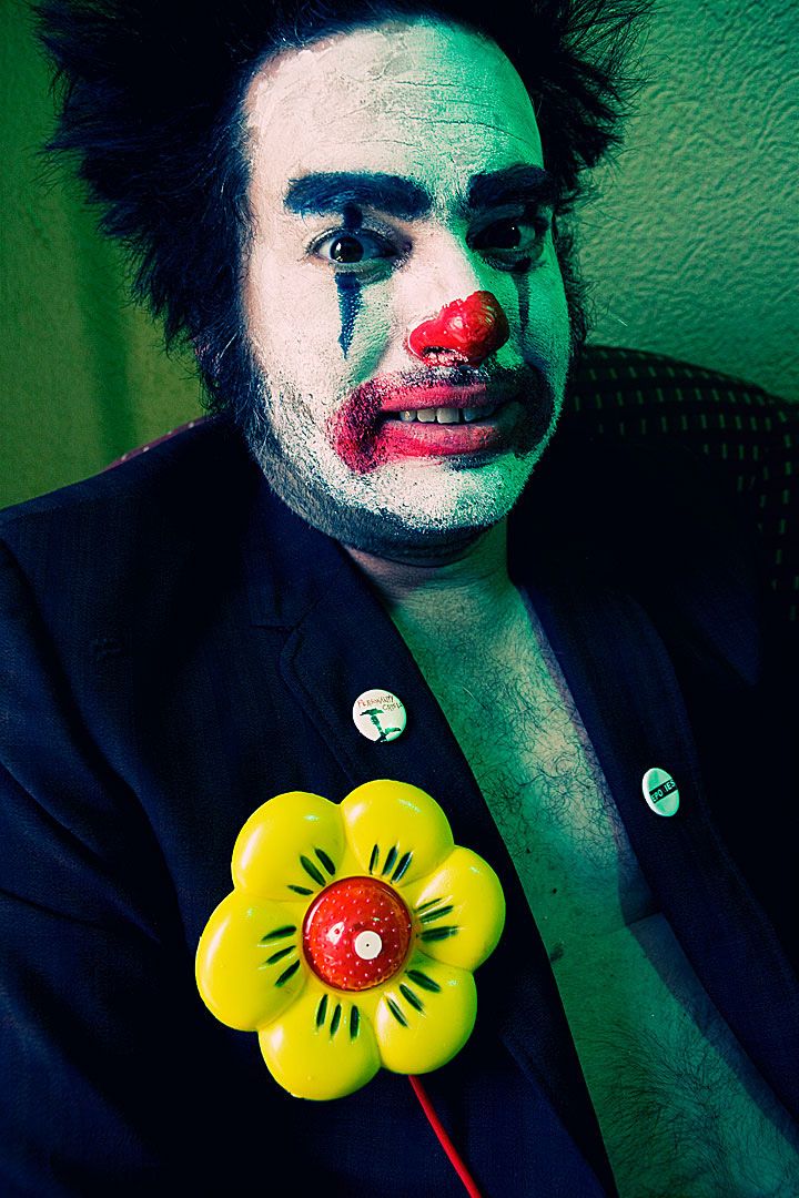 A series of dark artistic portraits with clown-like makeup featuring yellow flower props against a green backdrop.