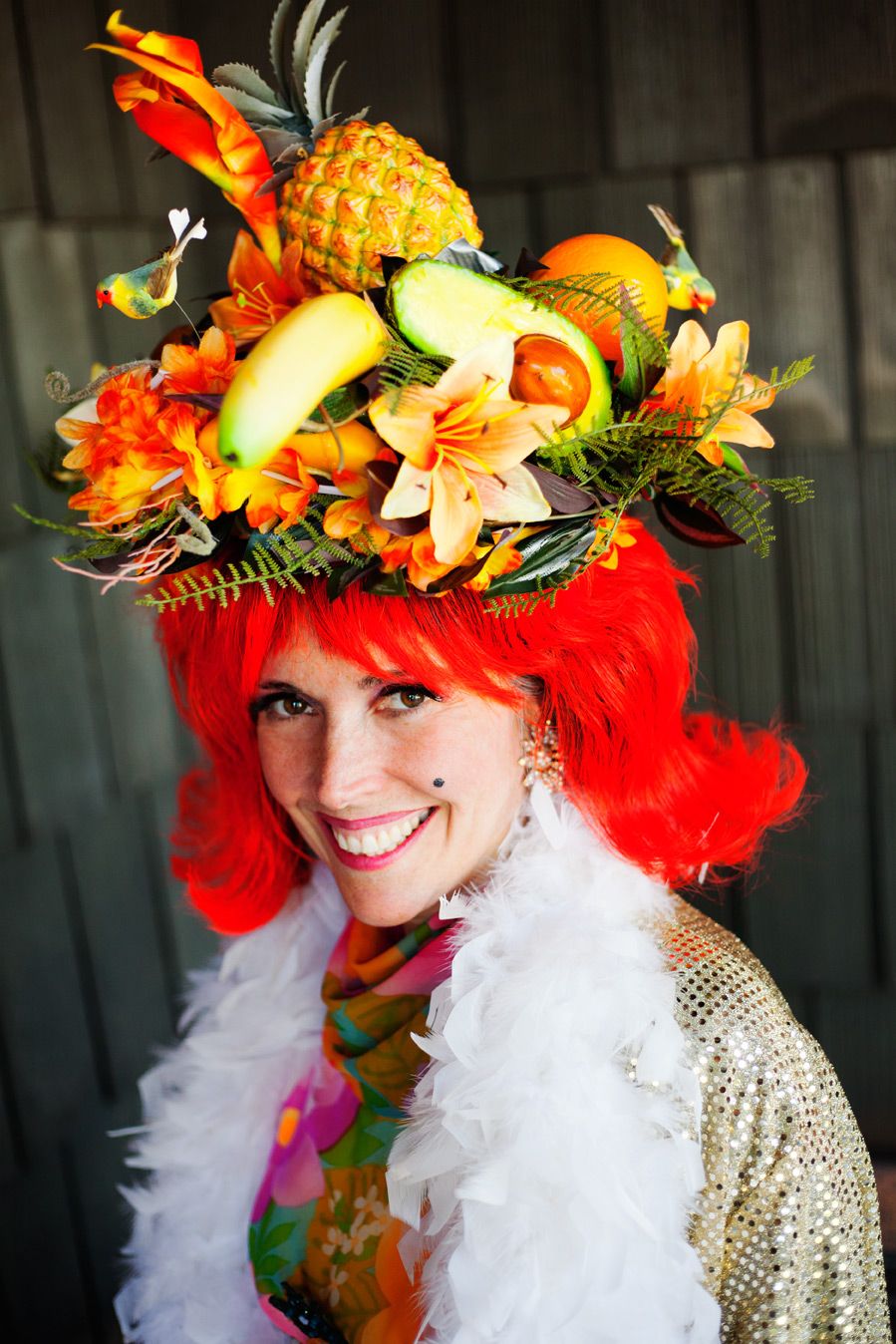 Colorful tropical floral headpiece with pineapples and flowers adorns a performer wearing a white feather boa and sequined outfit.
