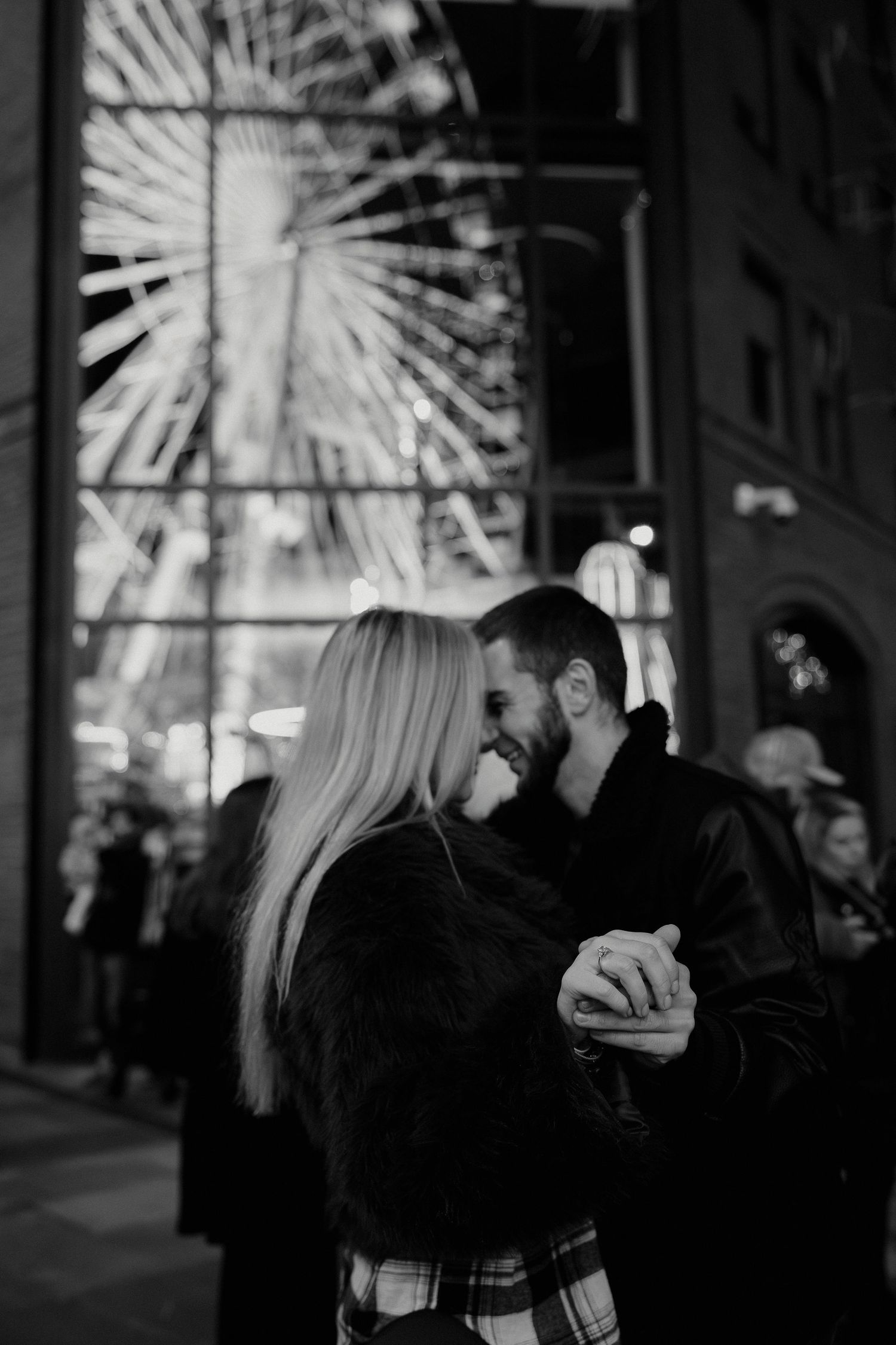 A couple playfully shares a marshmallow string game at an outdoor evening event with twinkling lights in the background.