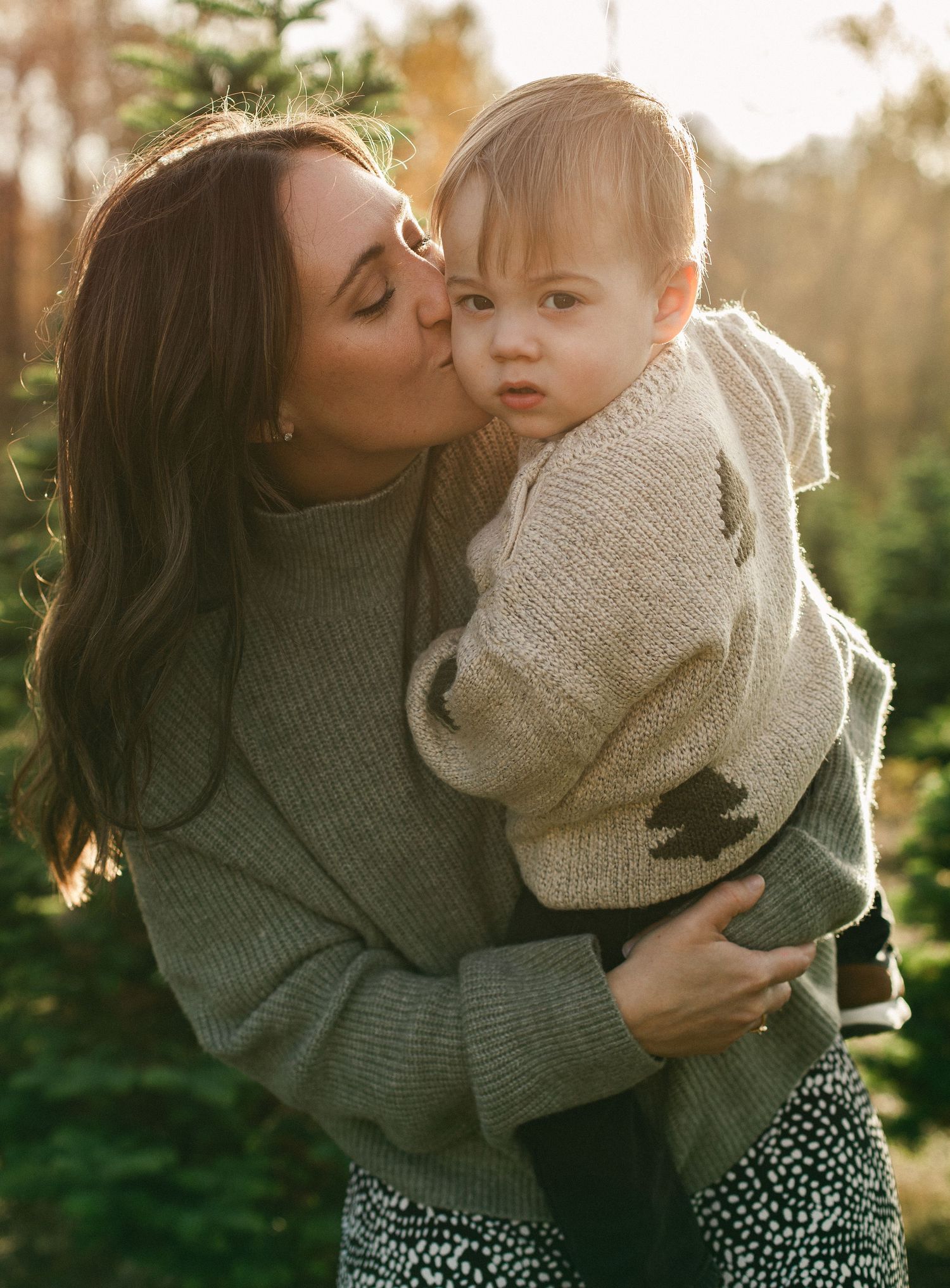 A mother and child in cozy sweaters share tender moments together in a sunlit outdoor setting.