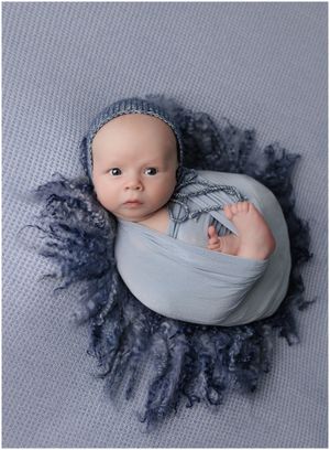 Sleeping newborn wrapped in soft blue fabric on textured backdrop in Austin newborn photography studio
