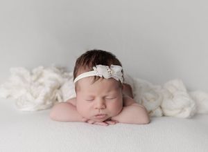 Sleeping newborn baby posed on soft cream blanket with headband in Austin newborn photography studio