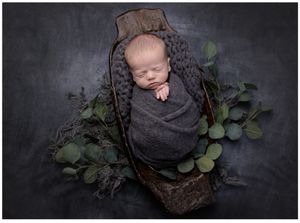 Newborn baby posed in wooden bowl with greenery and dark textured backdrop in Austin newborn studio