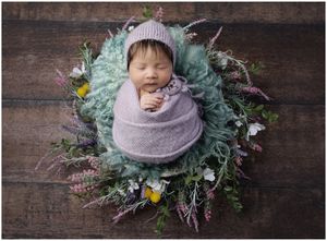Newborn baby wrapped in soft purple fabric posed with floral wreath on wood backdrop in Austin studio