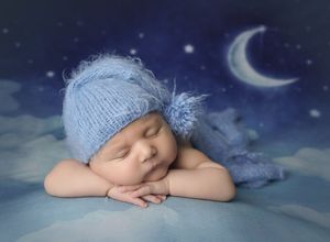 Sleeping newborn baby posed on blue fabric with moon backdrop in North Austin newborn photography studio