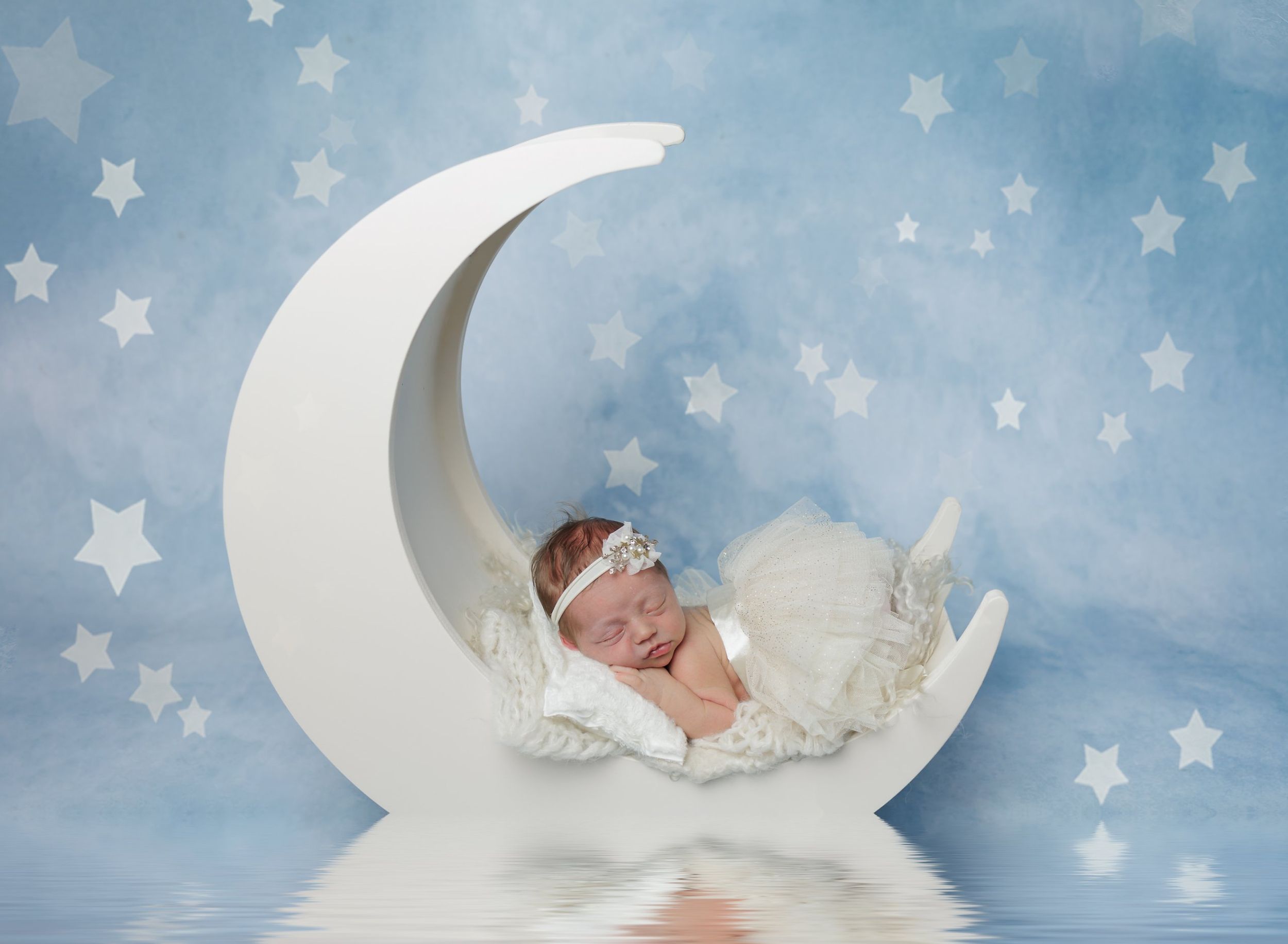 Newborn baby sleeping on crescent moon prop with star backdrop during studio newborn session in Austin
