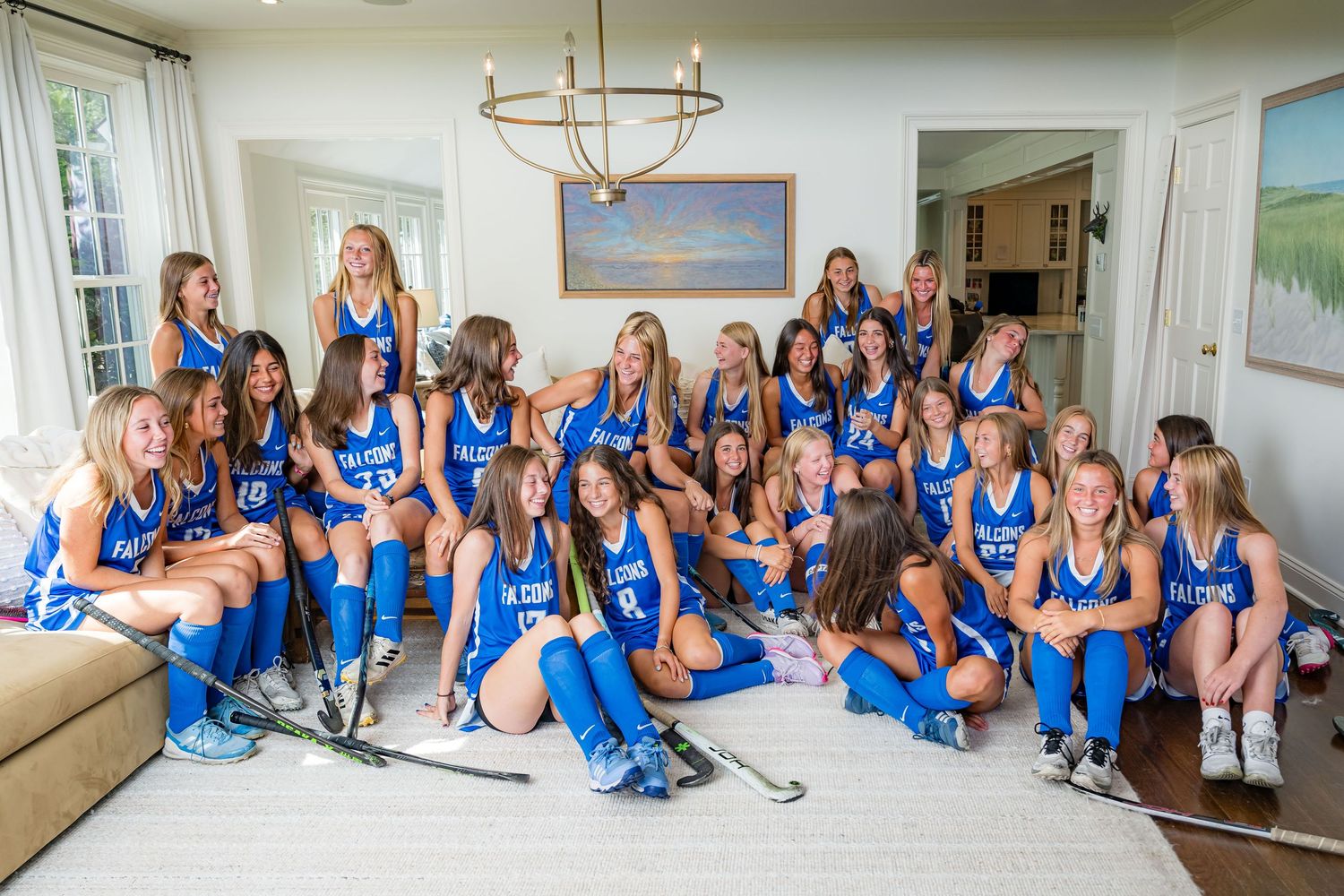 A group in matching blue uniforms sits together in a bright living room with a chandelier and coastal artwork.