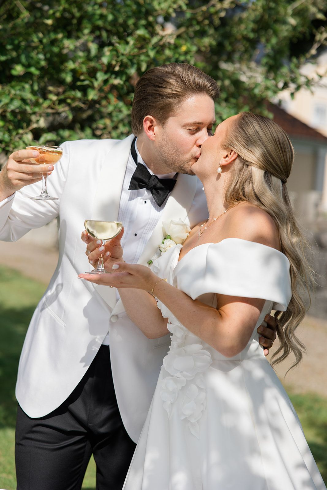 Joyful wedding party celebrates with confetti and white bouquets in front of an elegant estate.