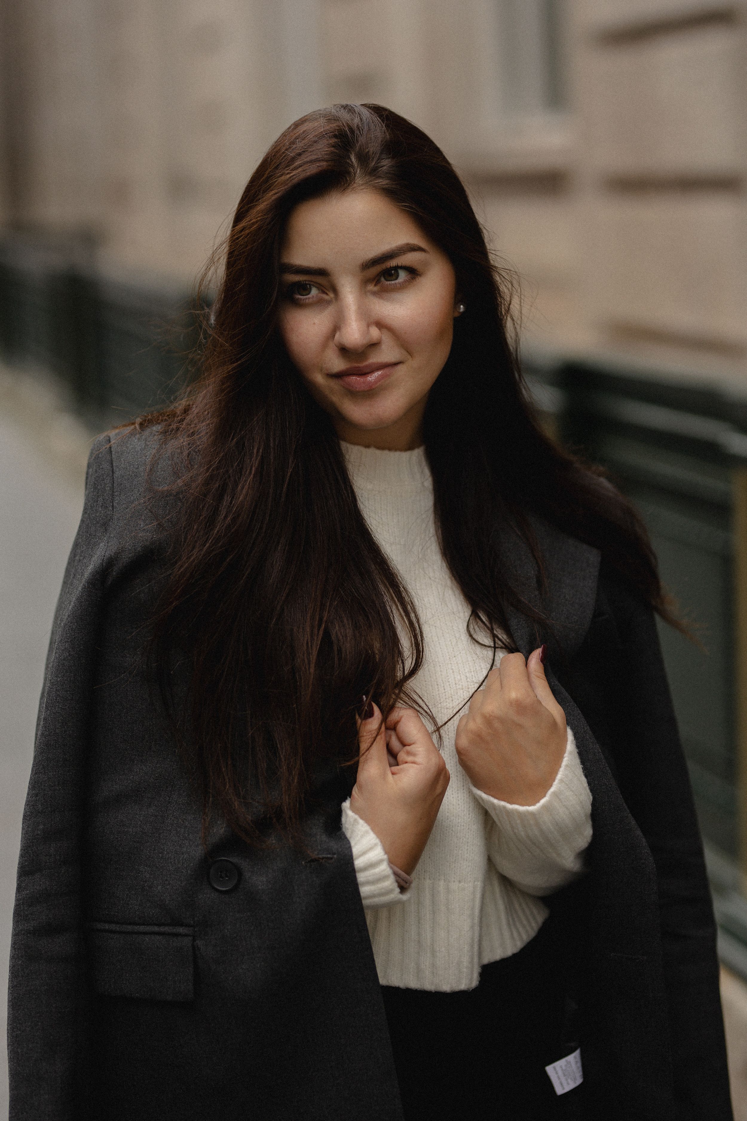A person with long dark hair wearing a black coat and white sweater poses playfully in a photo sequence.