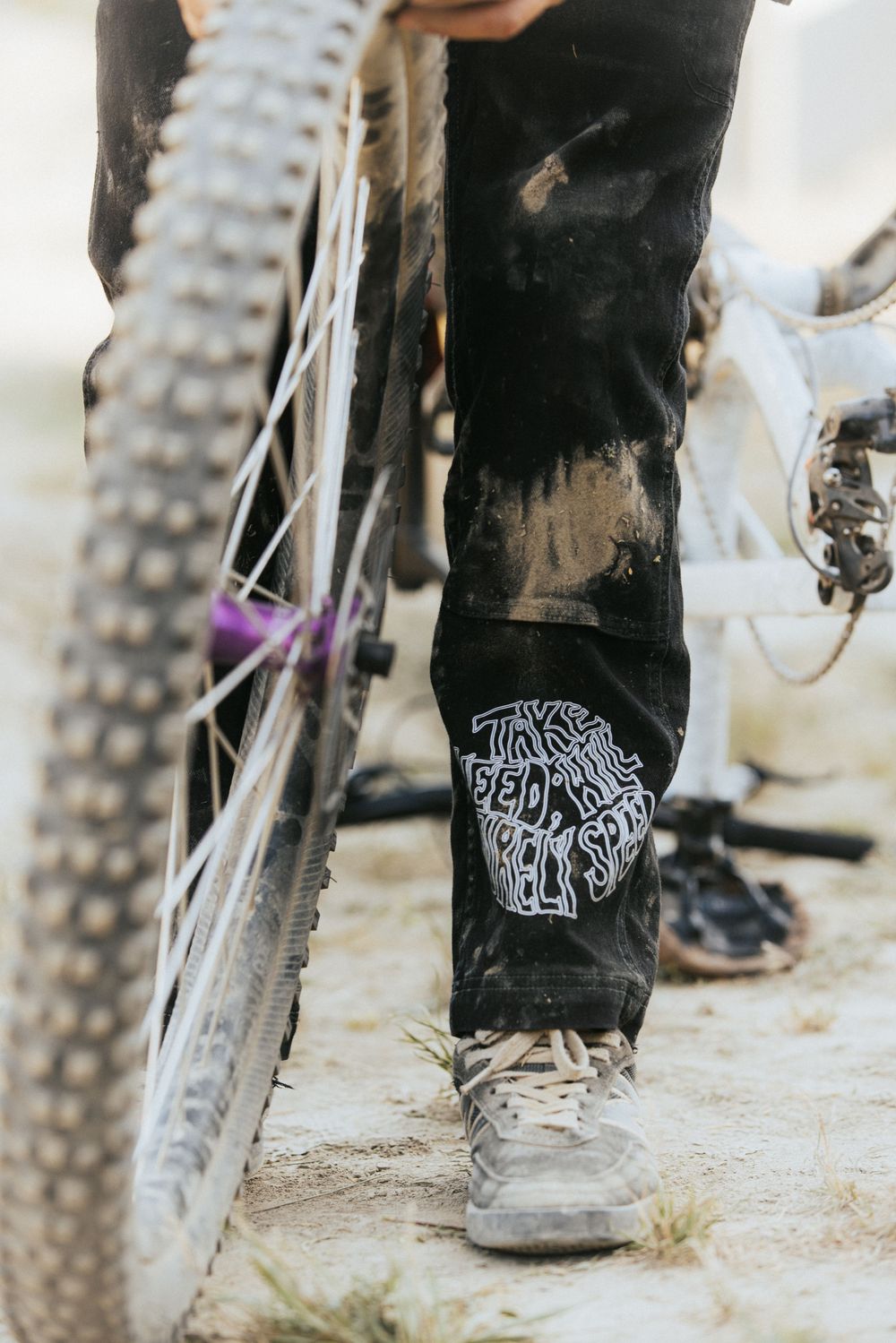 Close-up of mountain bike tires and rider's legs wearing black pants with graphic designs.