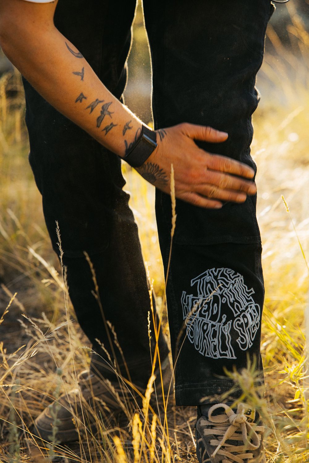 Close-up of hands against black clothing with decorative design detail in sunlit grass setting.