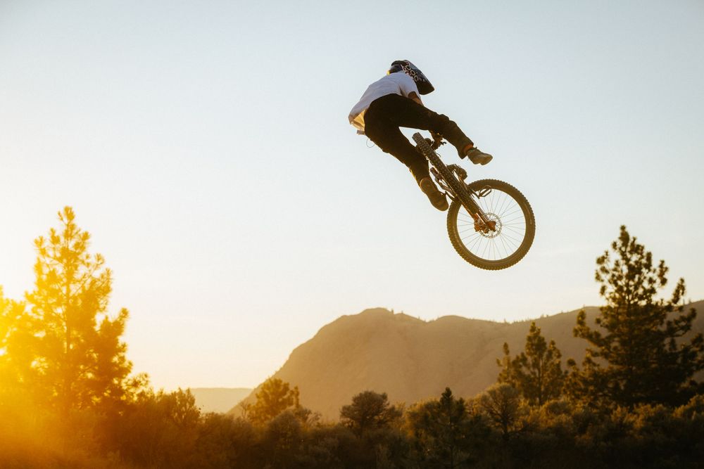 Silhouette of BMX rider executing aerial trick with mountains and golden sunset in background.