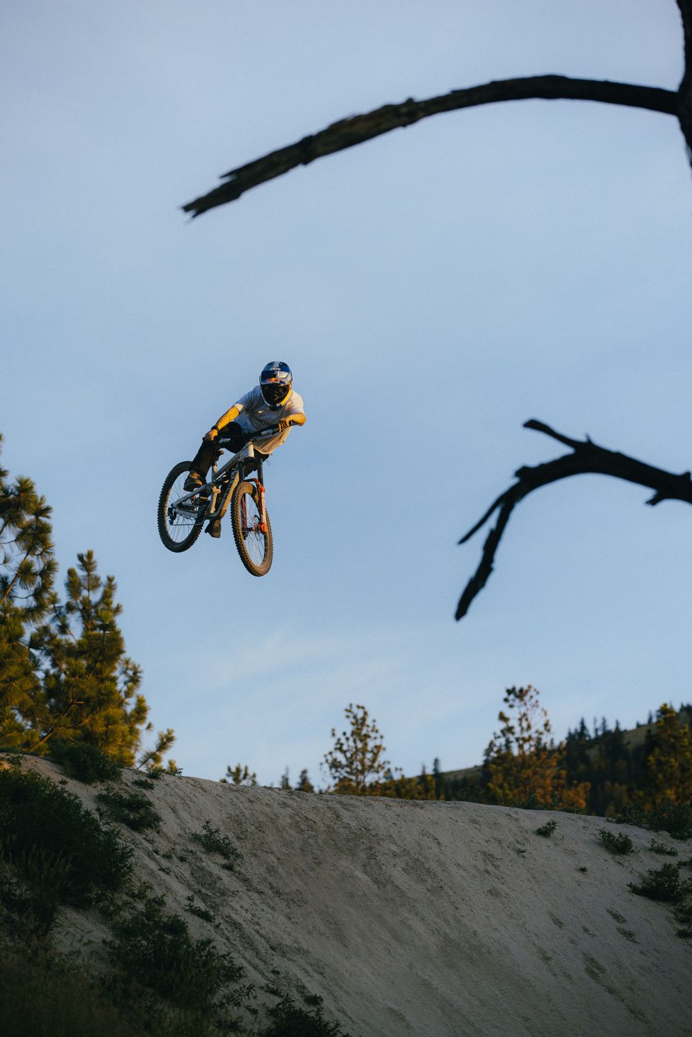 Sequence of a BMX rider performing a dramatic aerial trick jump off a dirt ramp against a blue sky.