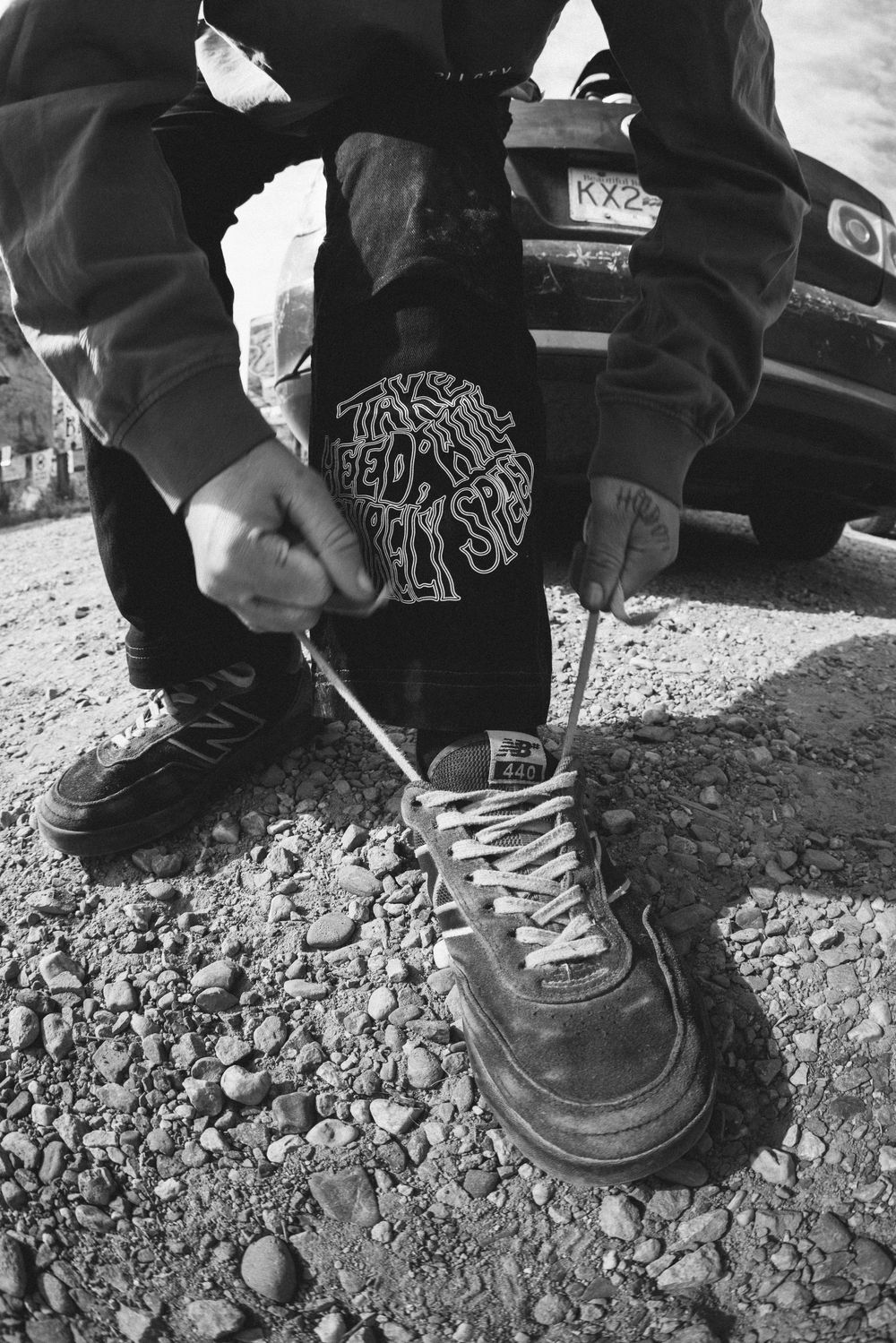 Black and white image of someone fixing or adjusting bike parts on rocky ground.
