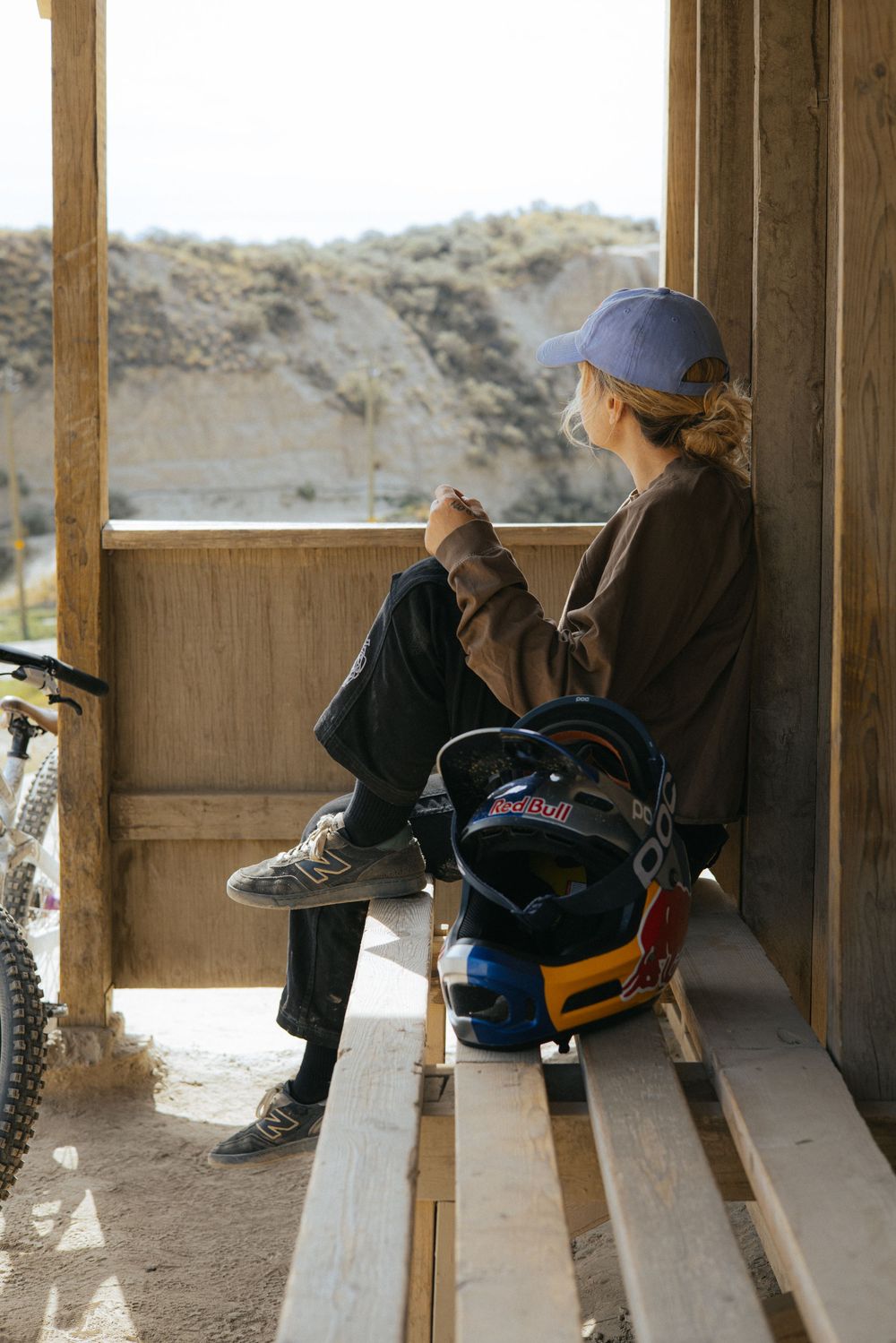 Group of people resting on wooden benches in an outdoor shelter overlooking desert landscape.