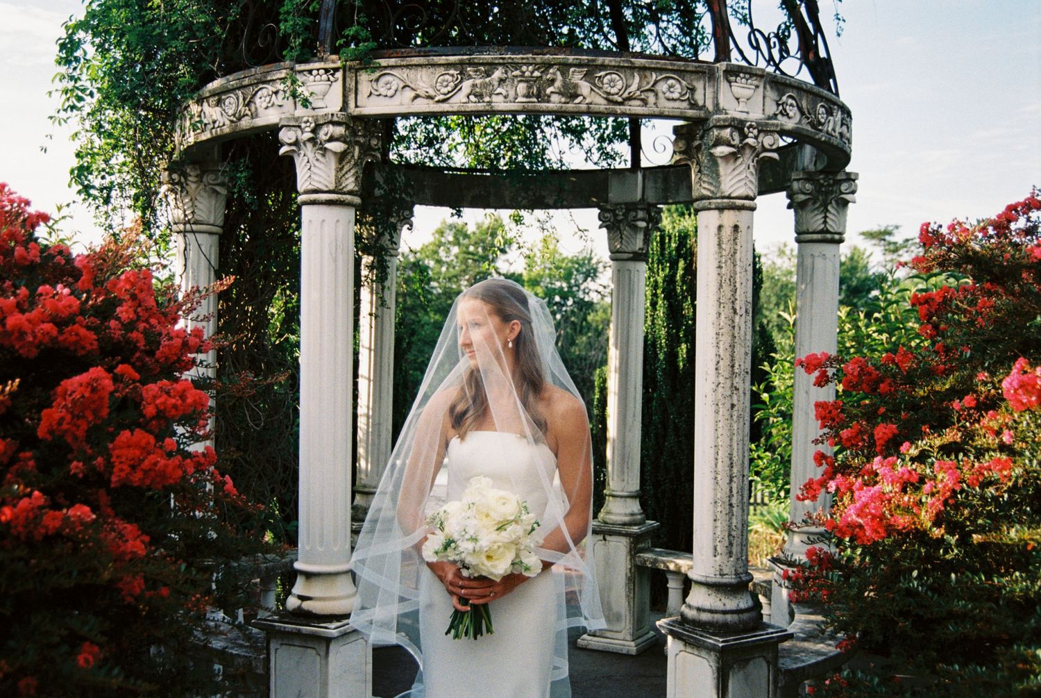A garden wedding venue with white columns and red flowering bushes creating a romantic outdoor setting.