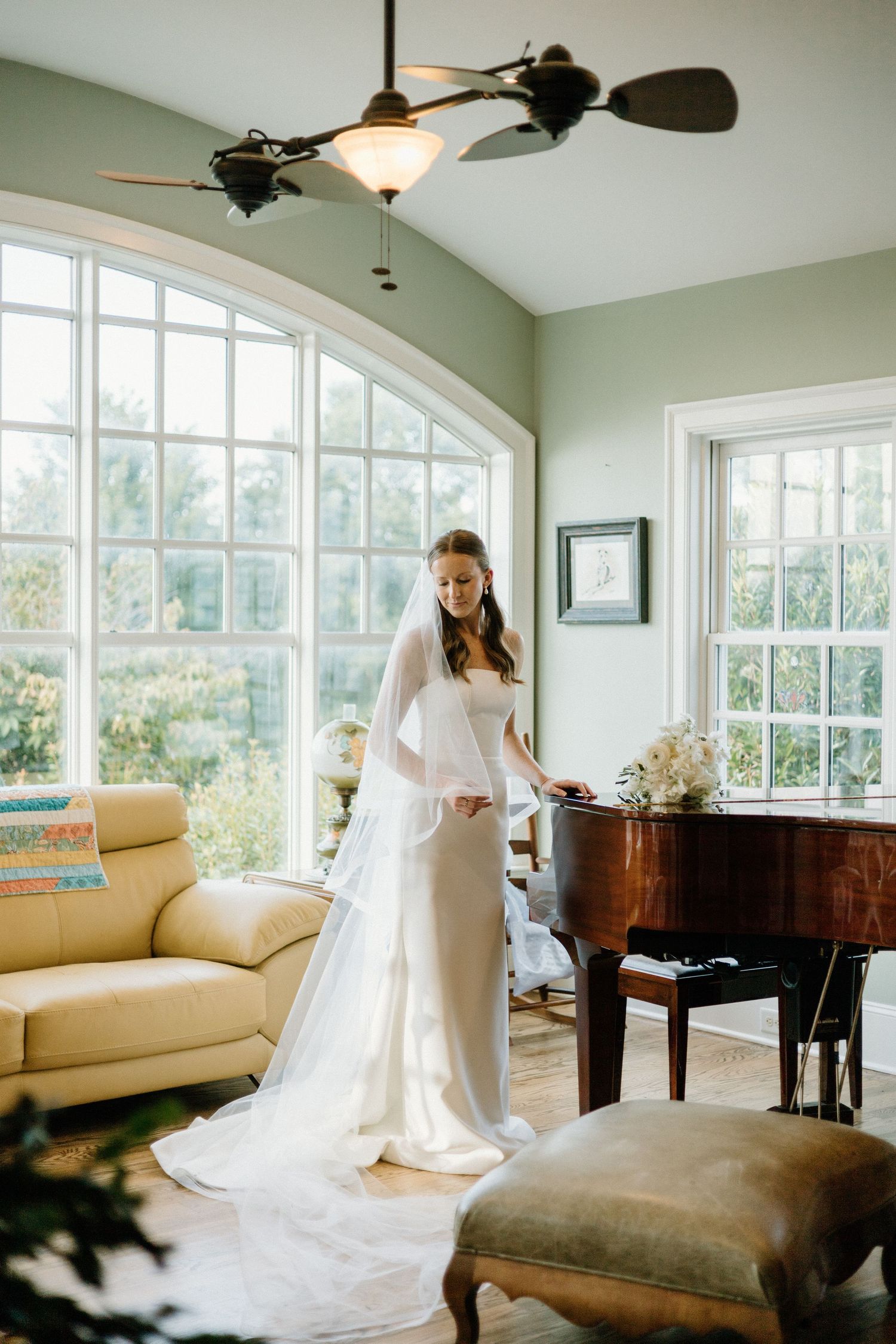 Elegant bridal portrait in a sunlit room with grand windows, a baby grand piano and unique dual-blade ceiling fan.