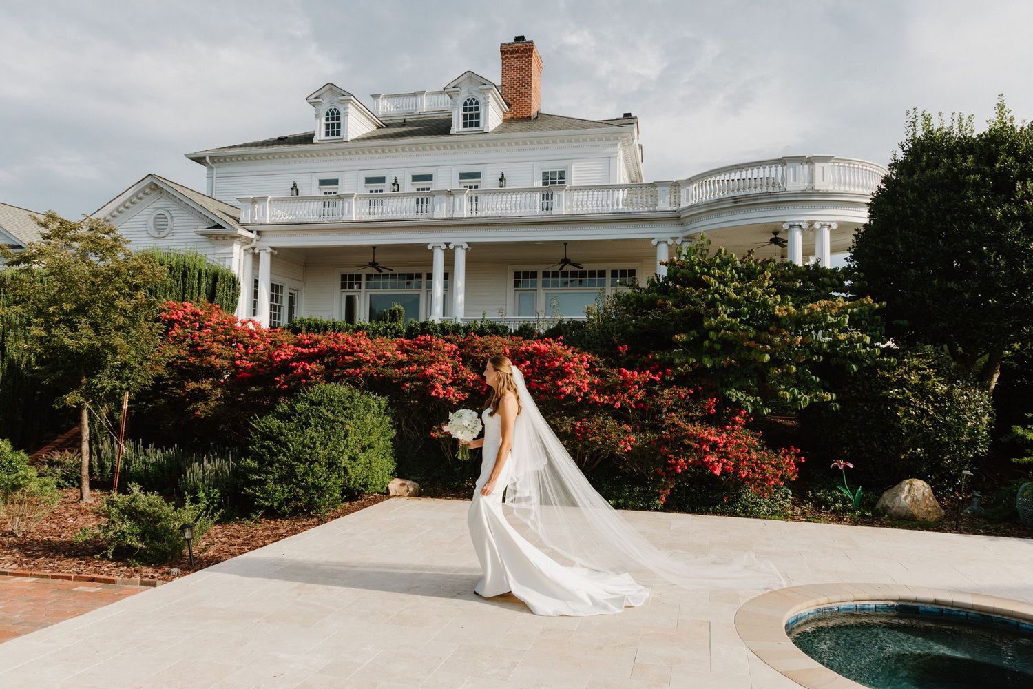 Elegant white wedding venue with manicured gardens and red flowering bushes creates a romantic outdoor setting.