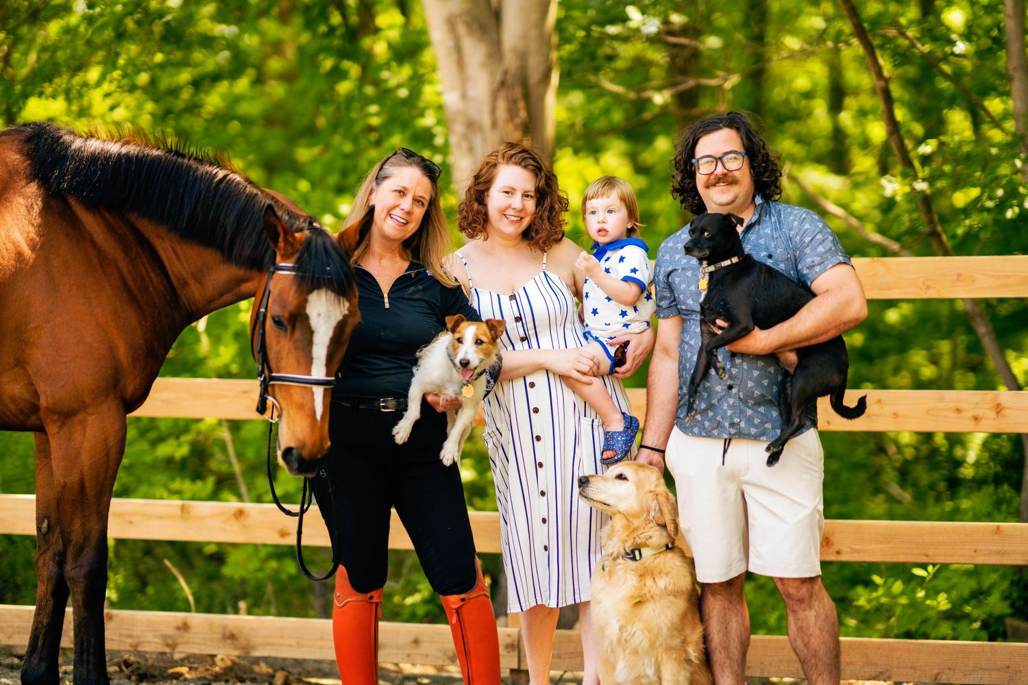 Family and their golden retriever dog pose together near wooden fence with a brown horse during outdoor photo session.