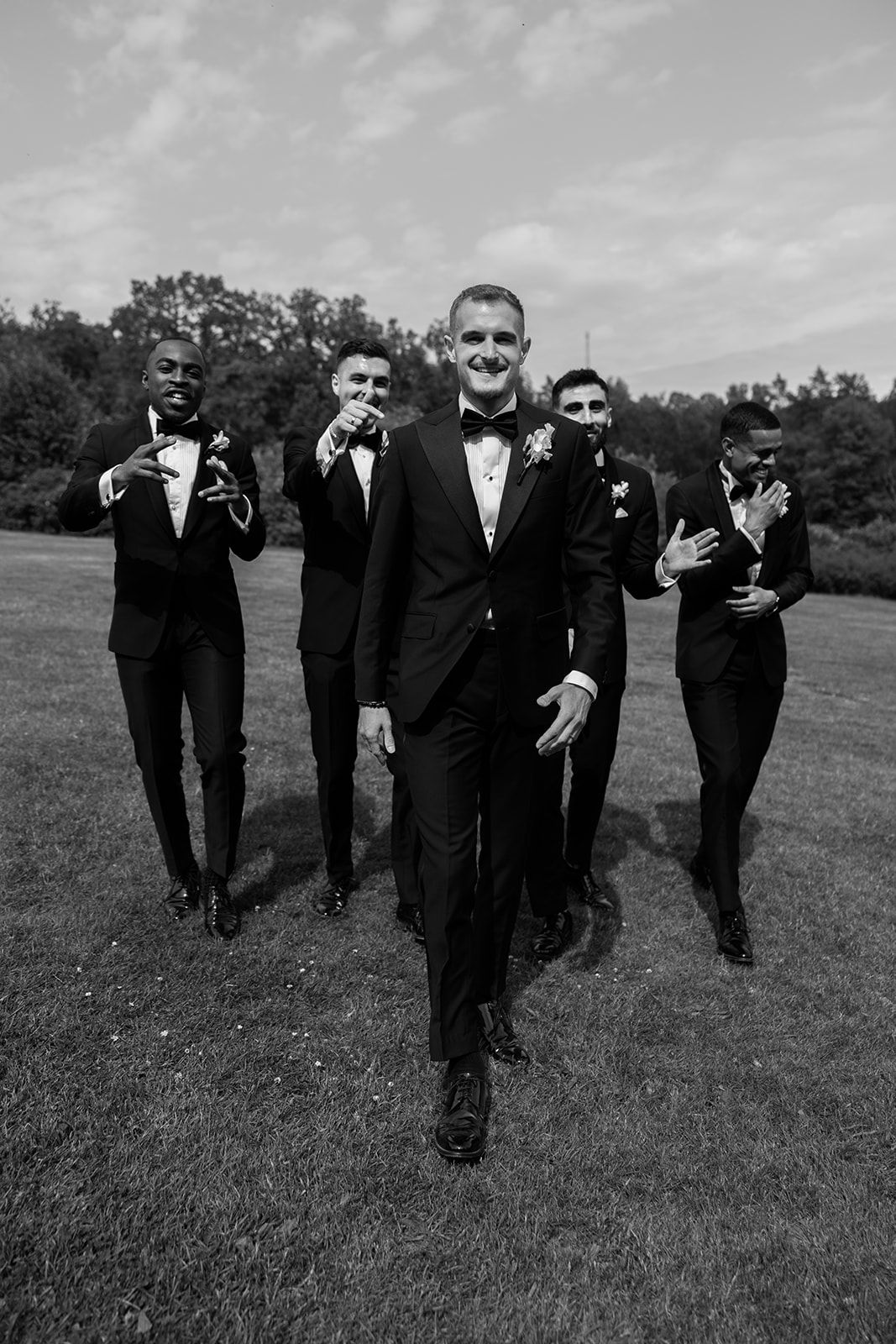 A group of groomsmen in black tuxedos walk together across a grassy field in a candid wedding photo sequence.