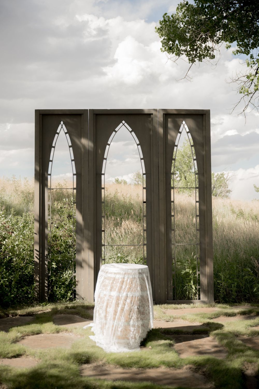 A sequence of four images showing a white wedding dress hanging in a rustic outdoor gazebo against a natural backdrop.