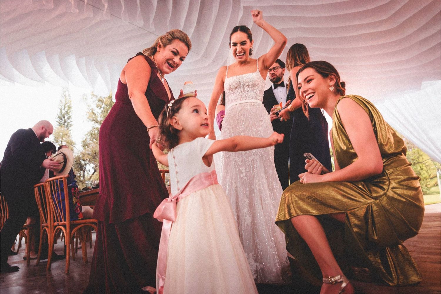 Wedding reception guests dance under a white tent during evening celebrations.