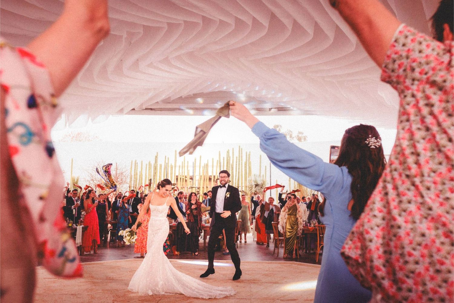 Panoramic view of a wedding reception tent filled with dancing guests and pink ambient lighting.