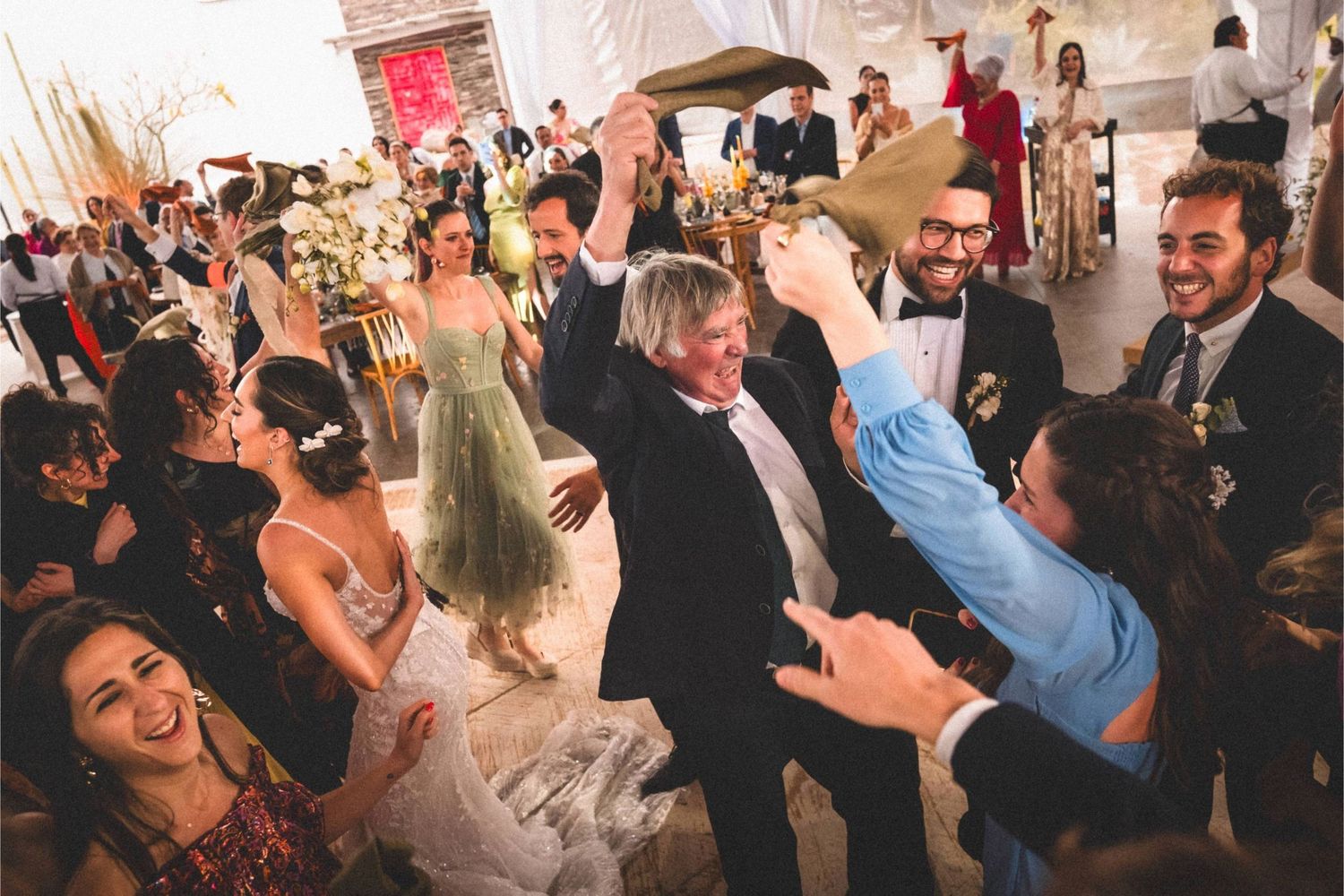 Wedding guests dancing and celebrating together on a crowded dance floor at a reception party.