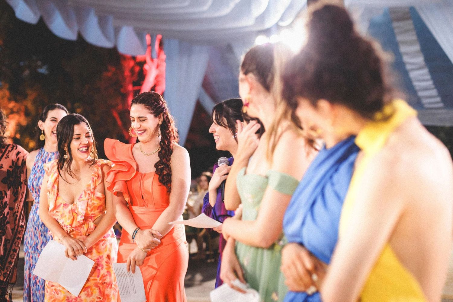 Wedding reception party with guests in colorful dresses dancing under white tent.