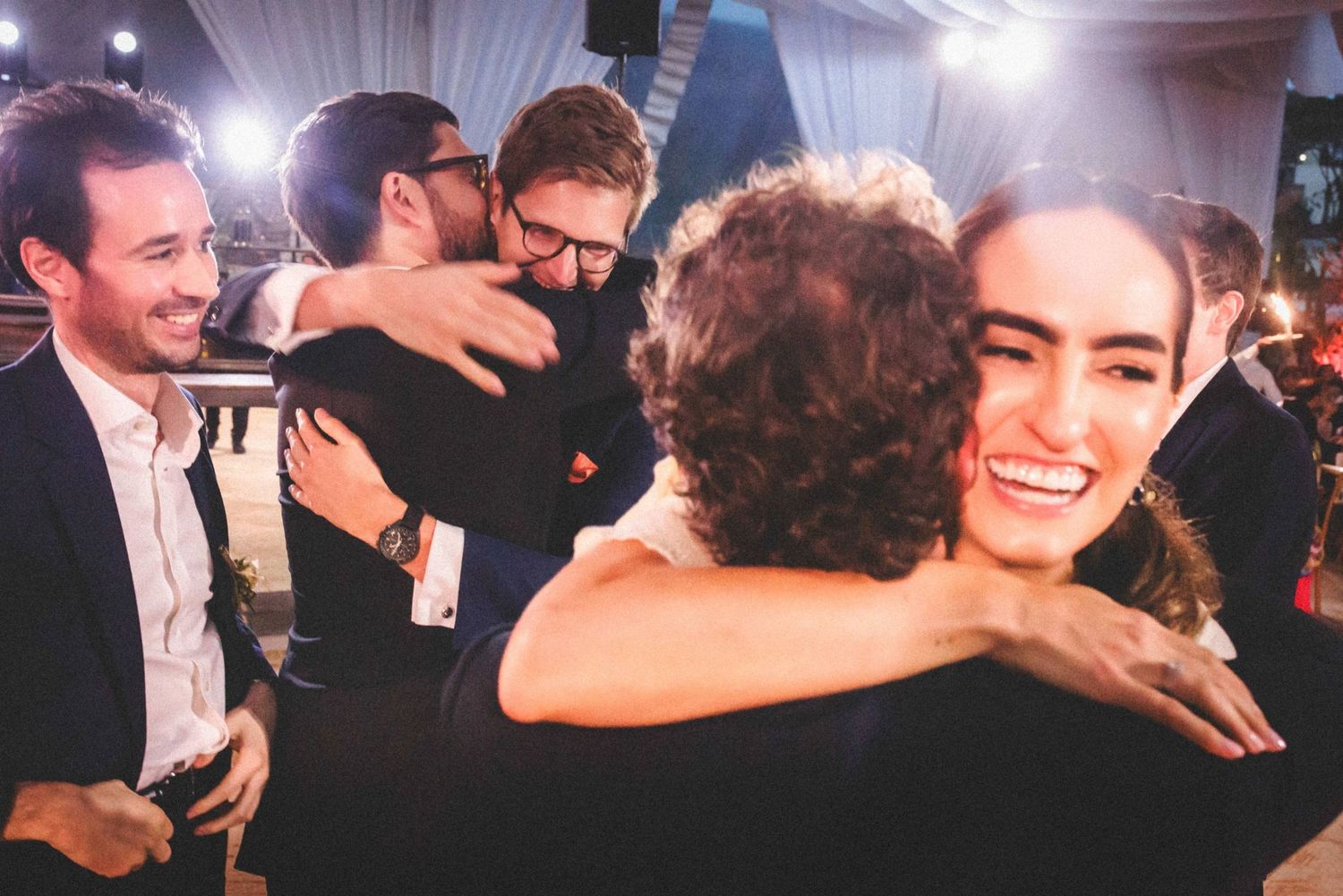 People sharing warm embraces and joyful moments at a celebratory indoor event with dramatic lighting.