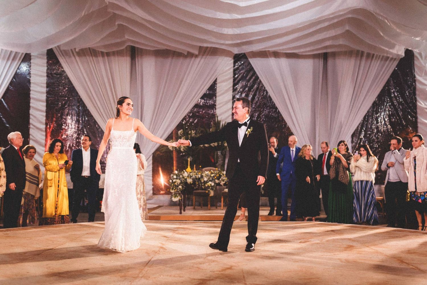Bride and groom having their first dance under elegant white draped fabric at an indoor wedding reception.
