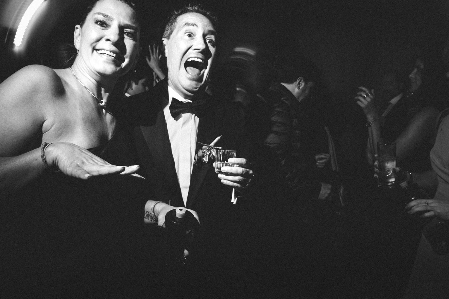 Black and white photograph of performers in formal attire singing and laughing on stage.