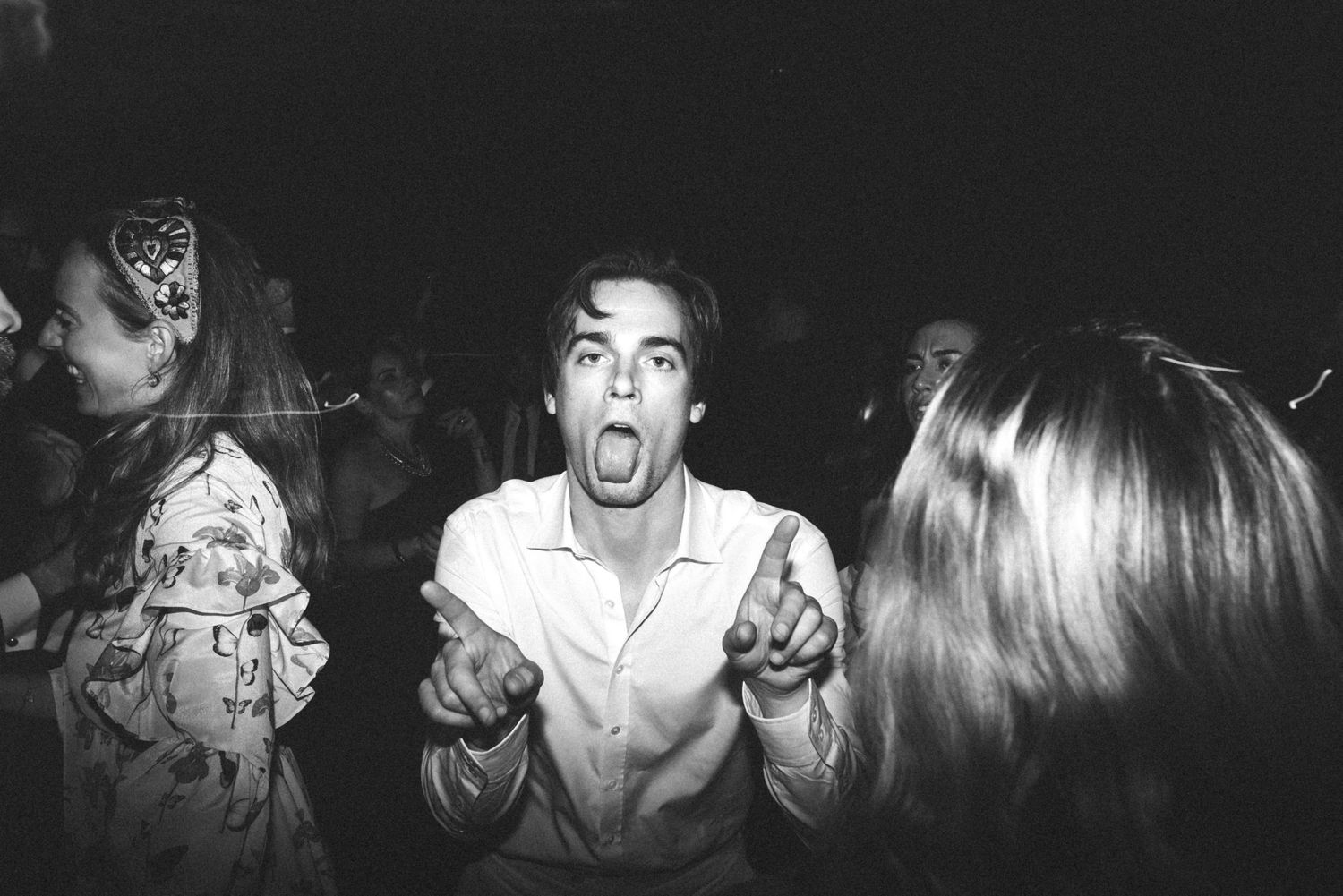 Black and white photo of energetic party guests dancing and celebrating at a nighttime event.