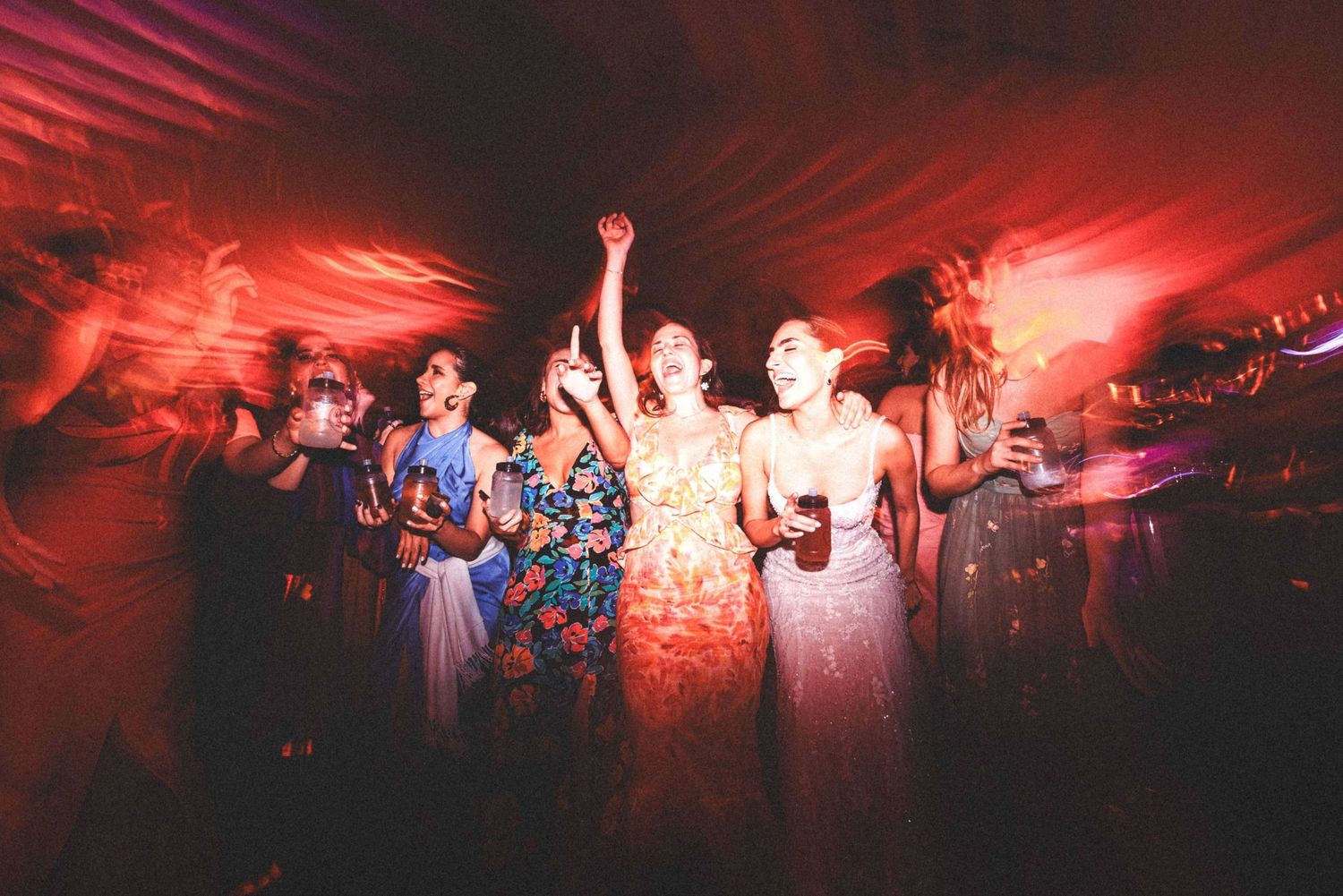 Wedding guests dancing and celebrating on a dance floor illuminated by dramatic red lighting at a reception party.