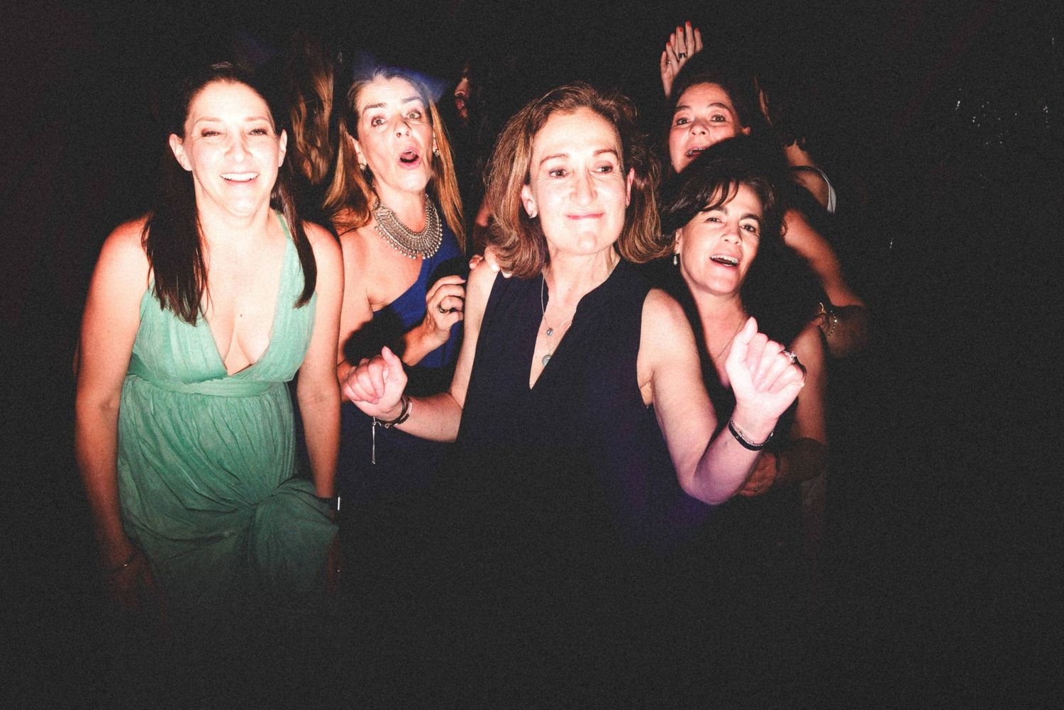Group of friends dancing and having fun at a nightclub in dark lighting with spotlights.
