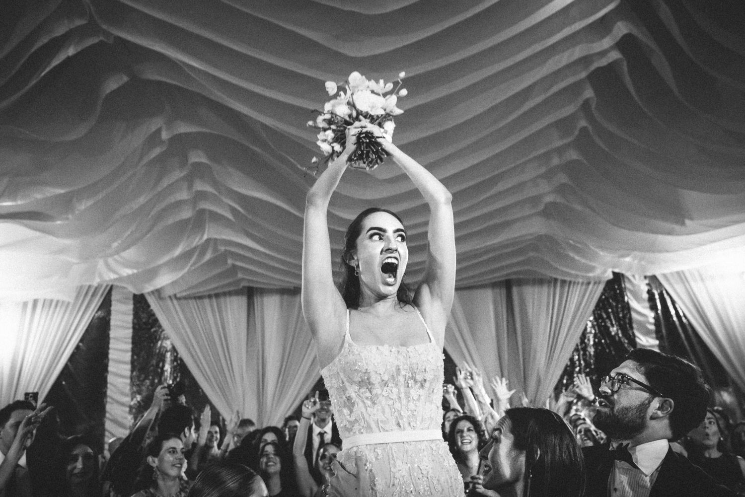 Wedding reception guests dancing and celebrating under elegant draped fabric ceiling decorations at an indoor venue.