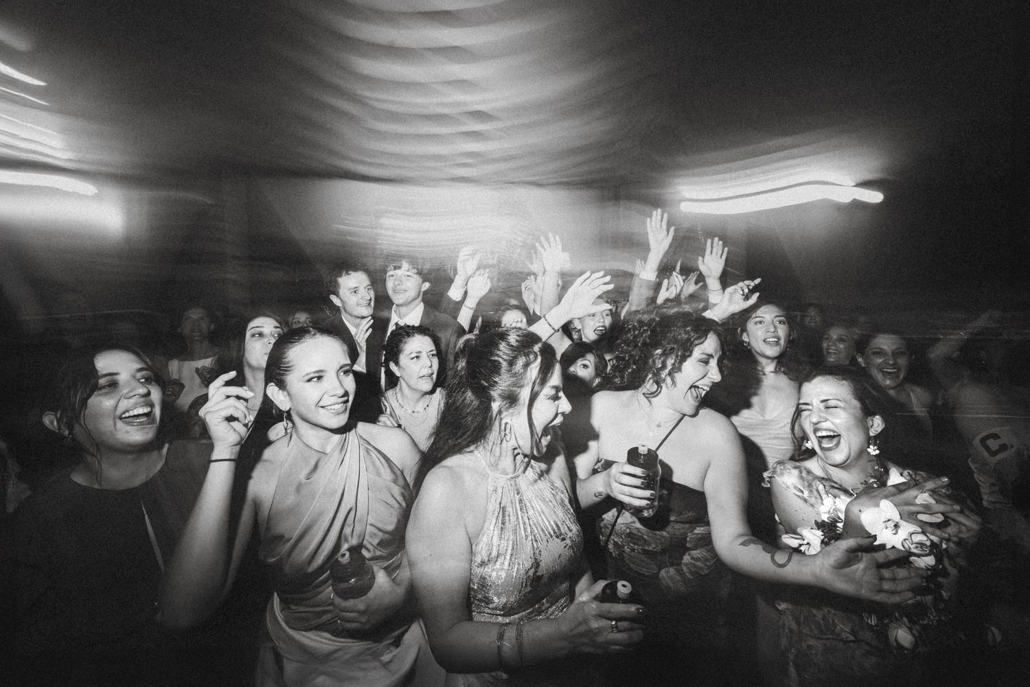 Black and white photo of an energetic crowd cheering and dancing at a nightclub or concert venue.