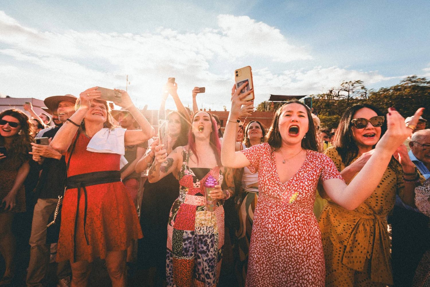 Crowd of festival goers dancing and celebrating at an outdoor music event during sunset.