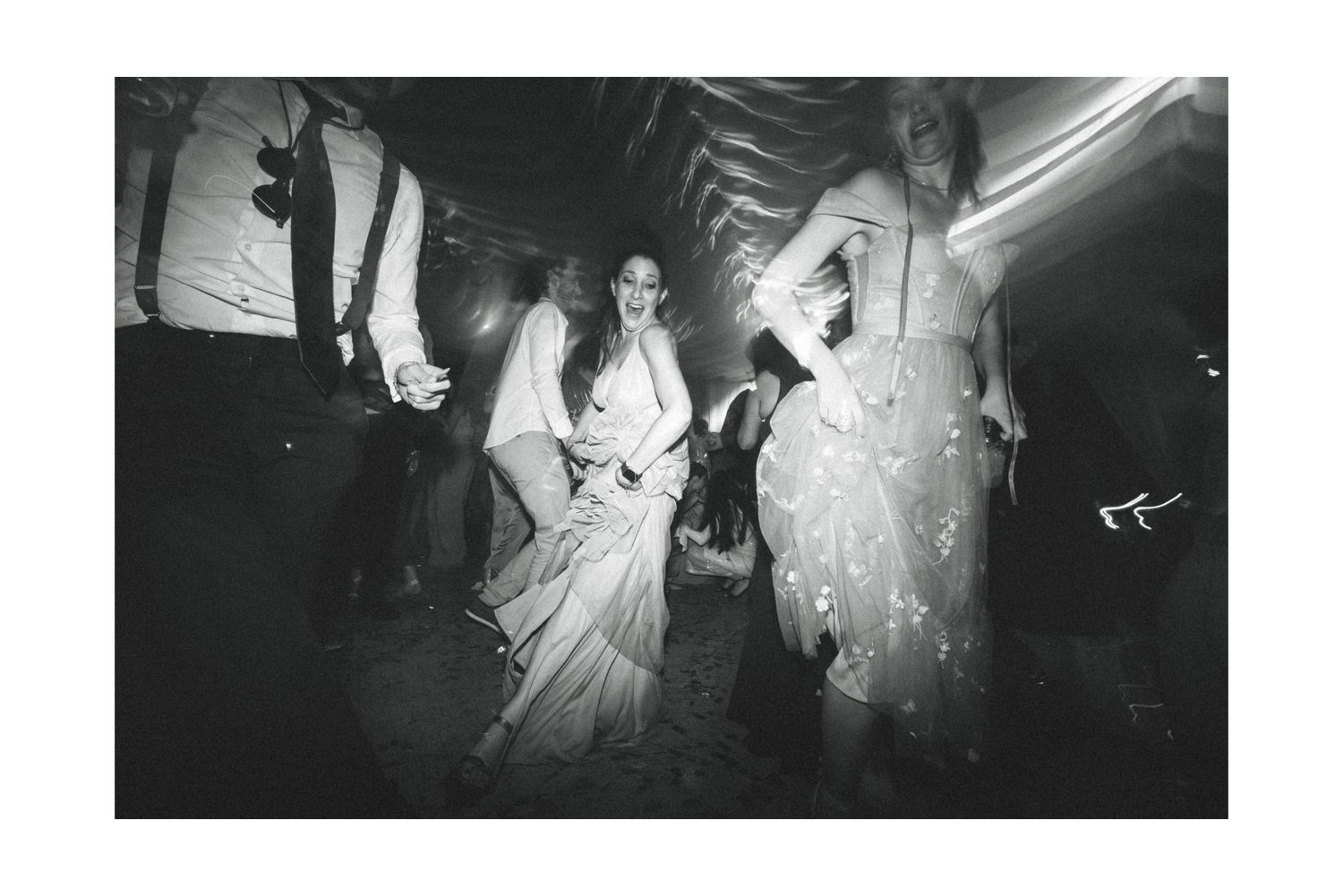 Black and white photograph of people in wedding attire dancing and celebrating at a reception party.