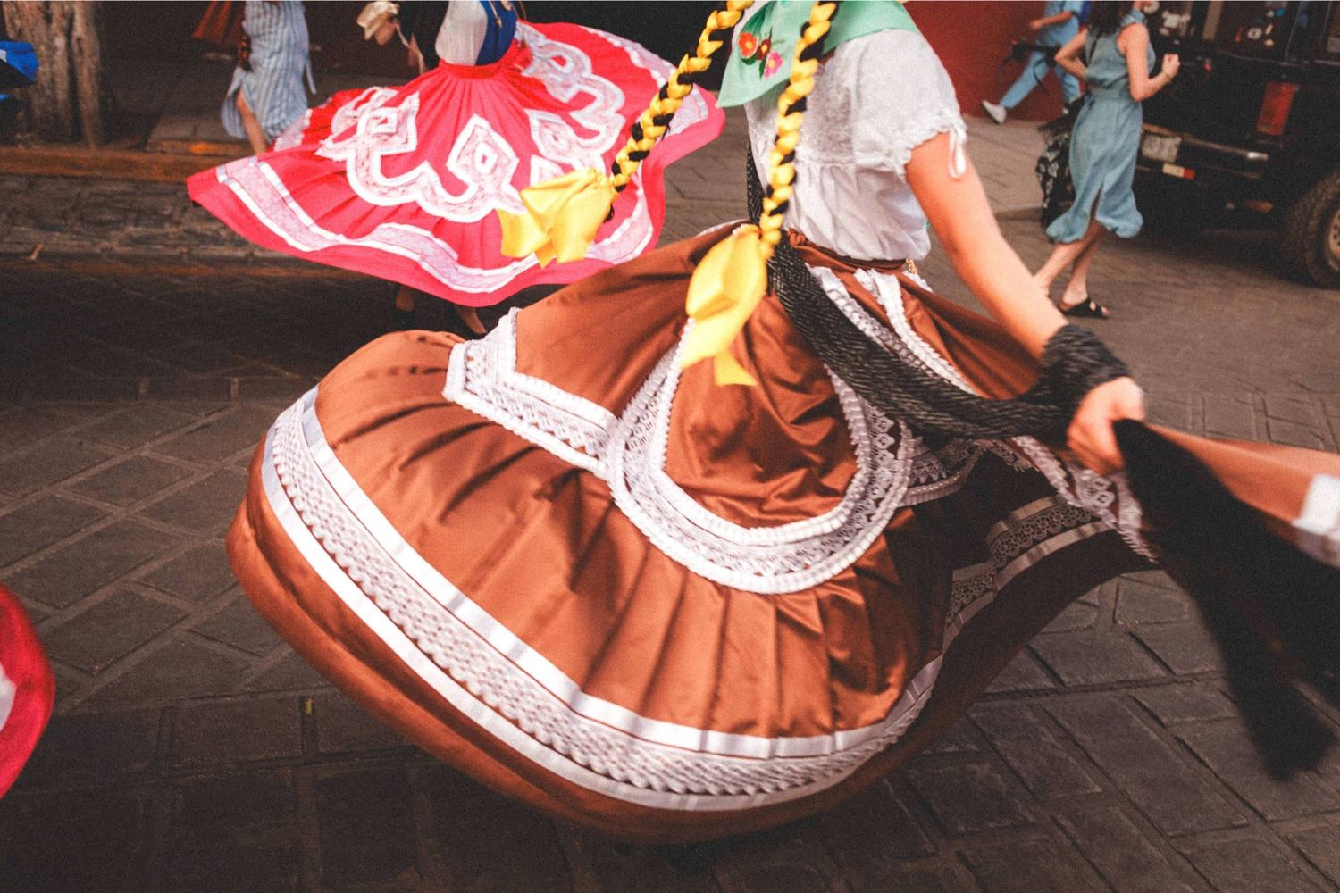 Dancers in traditional Mexican folklorico dresses with red and brown skirts perform at a cultural festival.