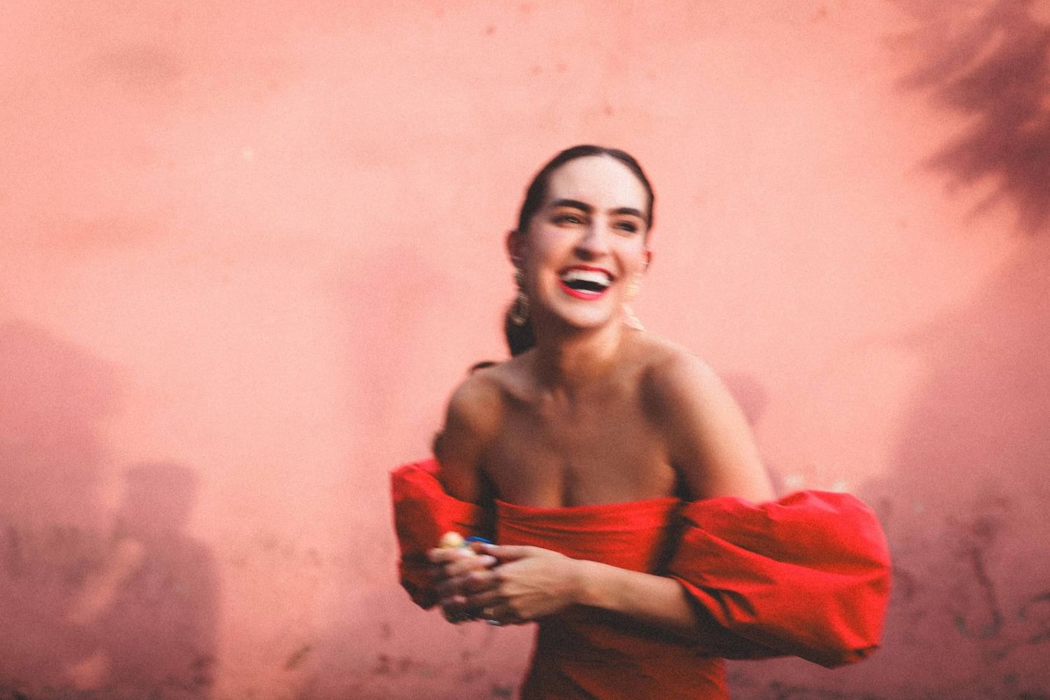 A person in a flowing red dress dances gracefully through pink-tinted fog creating an ethereal artistic scene.