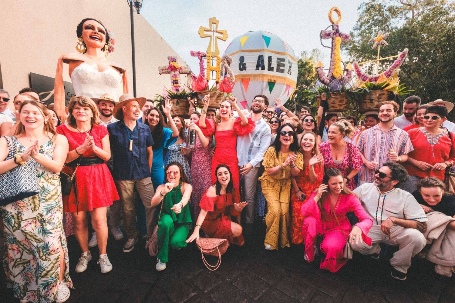A large group celebration outdoors with people gathered in festive red and colorful attire.