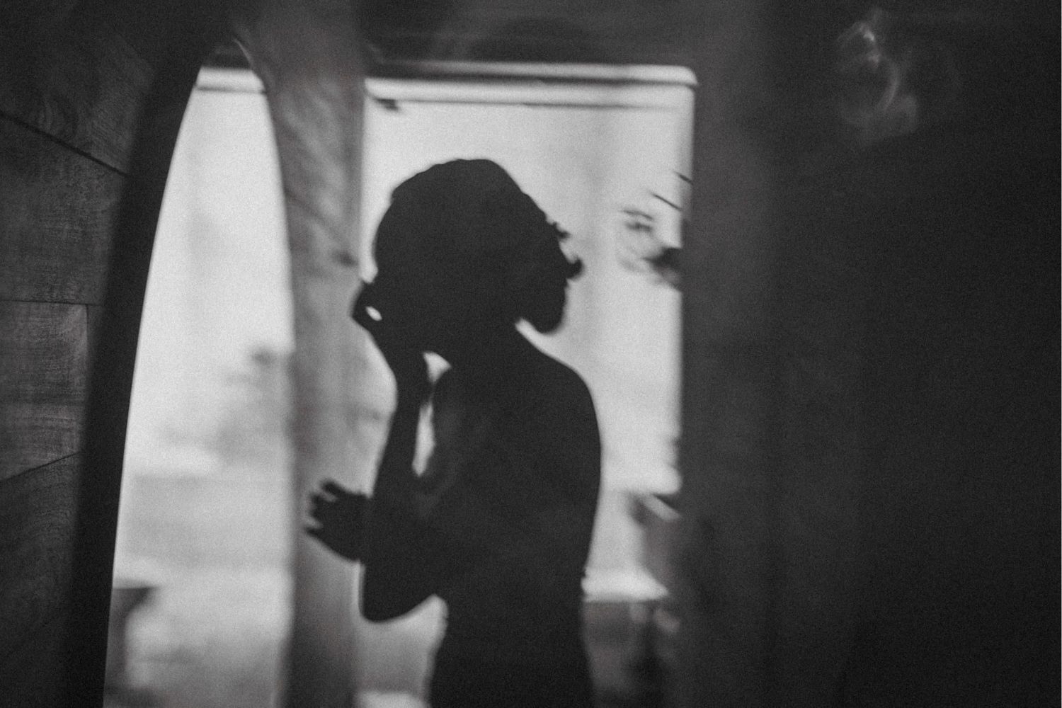 Silhouette of a couple in a romantic embrace against a window creating a dramatic black and white portrait.