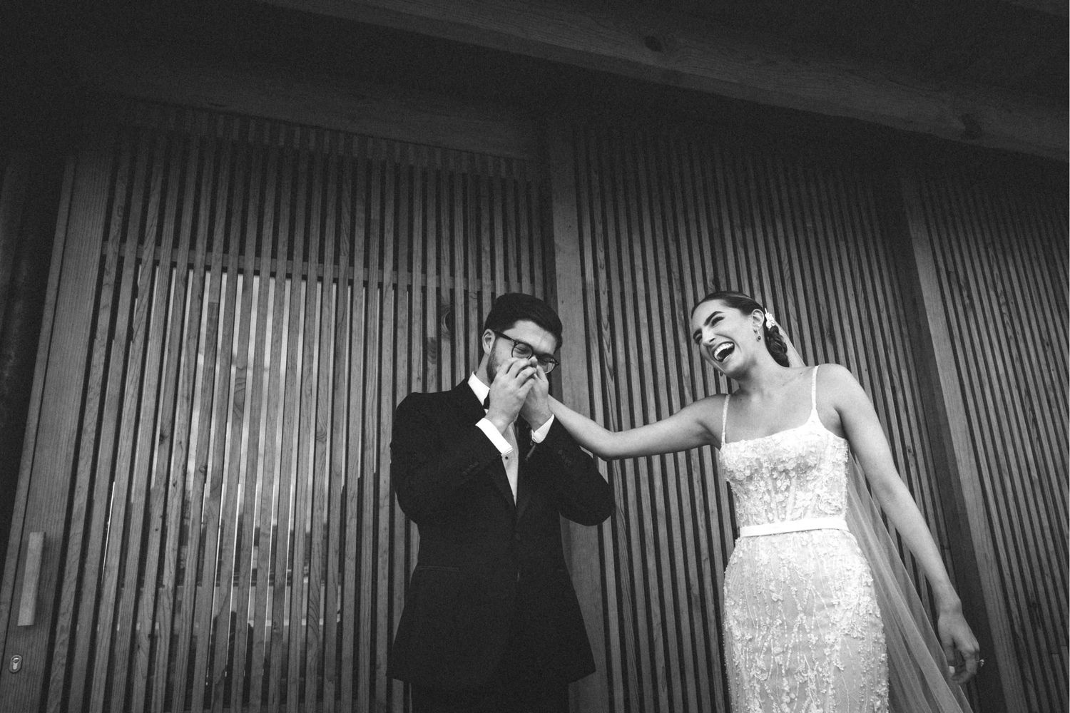 A couple in wedding attire walks down a dark corridor with dramatic lighting and shadows.