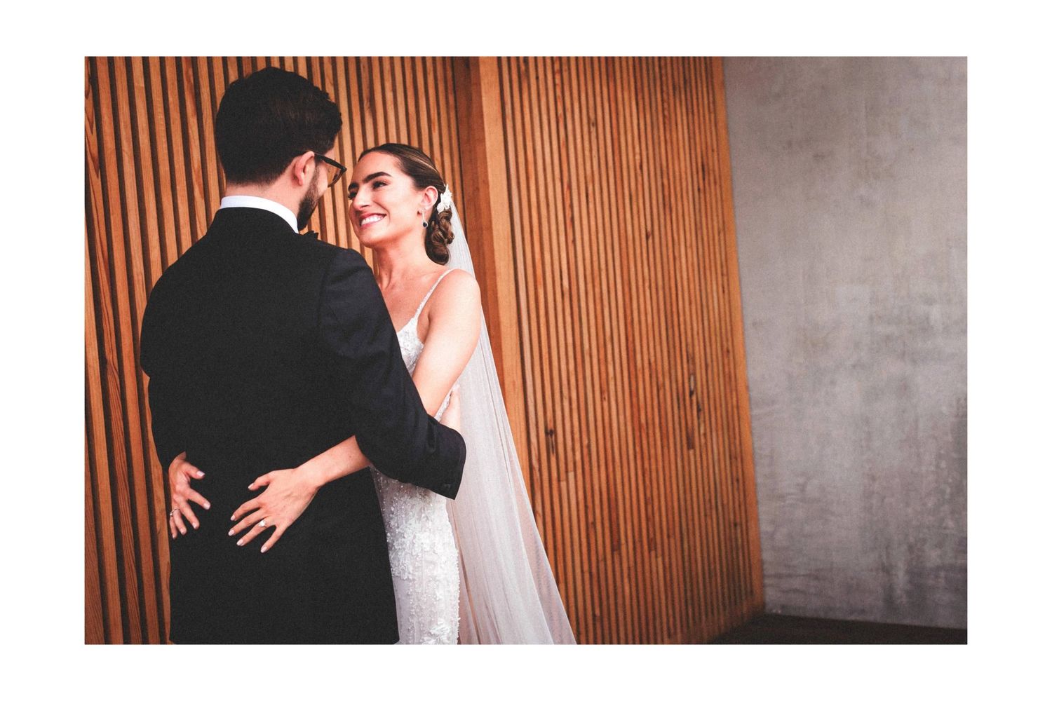 A couple in wedding attire embrace against a wooden slatted wall during their special day.