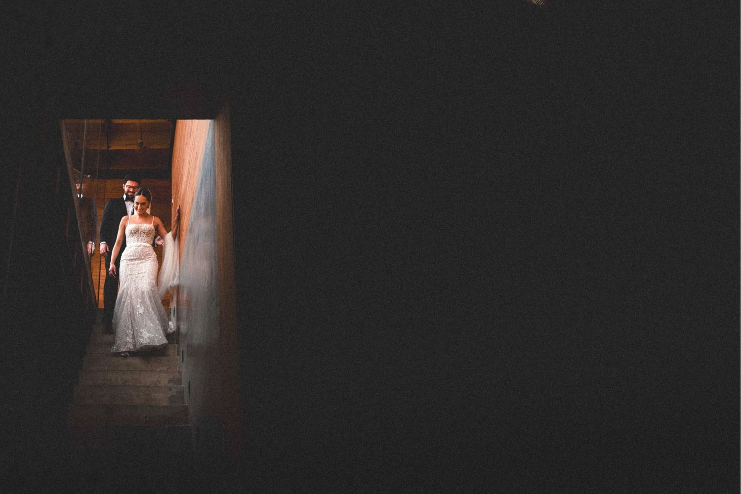 A bride in a white dress stands in a dimly lit hallway creating a moody atmospheric portrait.